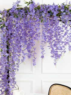 wistery purple flowers hang from the side of a white wall next to a chair