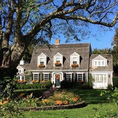 a white house with lots of windows and flowers in the front yard on a sunny day