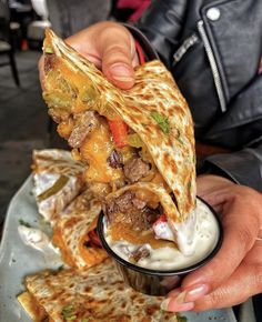 a person is holding up a pita sandwich and dipping it into a small bowl