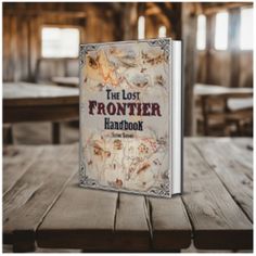 the lost frontier handbook book on a wooden table in a rustic setting with tables and benches