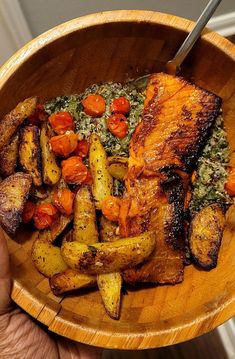 a person holding a wooden bowl filled with meat and veggies on top of it