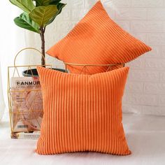 two orange pillows sitting on top of a bed next to a plant