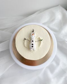 a white frosted cake with a snowman decoration on it's top sitting in a bowl