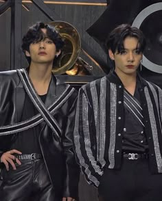 two men in black and white outfits standing next to each other with musical instruments behind them