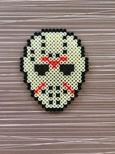 a beaded skull with red eyes on a wooden surface, in the shape of a cross - stitch pattern