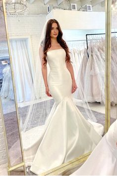 a woman standing in front of a mirror wearing a wedding dress