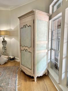 a white armoire sitting on top of a hard wood floor next to a window