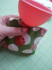 a hand holding a pink cup over a green and white flowered cloth with red flowers on it