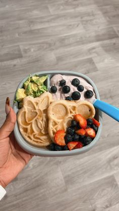 a person holding a plate with waffles, fruit and yogurt