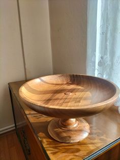 a wooden bowl sitting on top of a table next to a window in a room