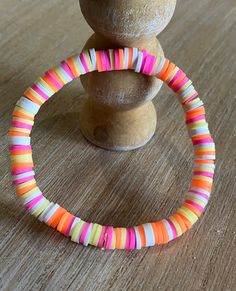 This vibrant and fun bracelet is made from colorful polymer clay disc beads, each stacked together to create a lively and playful pattern. The bracelet features a mix of bright pinks, oranges, yellows, and whites, making it the perfect accessory to add a pop of color to any outfit. Lightweight and stretchy, it's comfortable to wear all day long, whether you're dressing up for a special occasion or adding some flair to your everyday look. This bracelet is a great choice for anyone who loves unique, handmade jewelry with a cheerful and energetic vibe. Multicolor Plastic Stretch Bracelet For Beach, Playful Orange Bracelets For Beach, Vibrant Pink Beaded Bracelet For Beach, Playful Orange Bracelets With Colorful Beads, Multicolor Plastic Beaded Bracelet For Beach, Multicolor Plastic Beaded Bracelets For Beach, Playful Multicolor Heishi Beads Stretch Bracelet, Sunset Bracelet, Clay Bead Bracelets