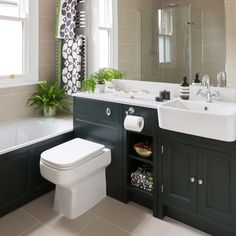 a white toilet sitting next to a bath tub in a bathroom under a window with curtains