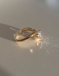 a gold ring with a single diamond in the center on a white surface, surrounded by sunlight