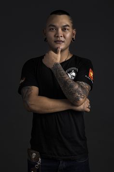 a man with tattoos and piercings poses for a photo in front of a black background