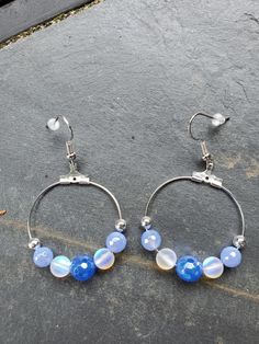 These earrings are made with blue agate beads plated with a silver coating that provides a lot of shine. The clear stones are moonstone beads that flash with color. They are made so that the hoops face forward. Blue Round Earrings With Gemstone Beads, Blue Hoop Earrings With Natural Stones, Blue Moonstone Round Earrings, Blue Moonstone Earrings With Natural Stones, Blue Natural Stone Dangle Hoop Earrings, Face Forward, Moonstone Beads, Clear Stone, Blue Agate