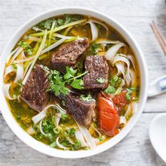 a bowl of beef and vegetable soup with chopsticks next to it on a table