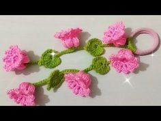 crocheted pink flowers with green leaves on white table top next to pair of scissors