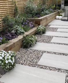 an outdoor garden with stone walkways and flowers in the foreground, next to a wooden fence