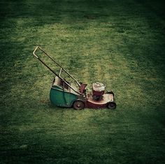 a lawn mower sitting on top of a green field next to a trash can