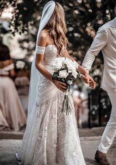 a bride and groom walking down the street holding hands in their wedding day attire, dressed in white