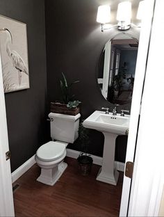 a white toilet sitting next to a sink in a bathroom under a painting on the wall