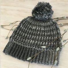 a knitted beanie hat sitting on top of a wooden table next to dried flowers