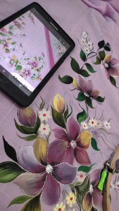 a tablet computer sitting on top of a table next to a flowered cloth with flowers painted on it