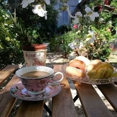 a cup of coffee sitting on top of a wooden table next to a bowl of fruit