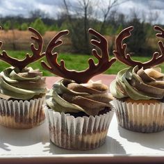 three cupcakes with chocolate frosting and deer antlers on top are sitting on a table