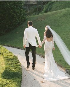 a bride and groom walking down a path holding hands