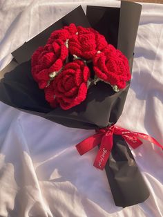 a bouquet of red crocheted roses in a black paper bag on a white sheet