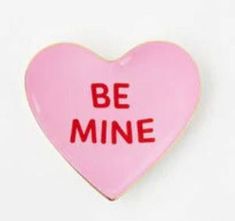 a pink heart shaped pin with the words be mine on it