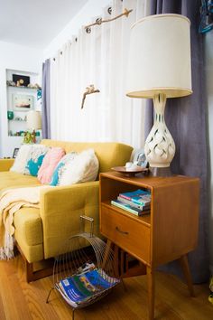 a living room filled with furniture and a lamp on top of a wooden table next to a yellow couch