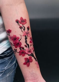 a woman's arm with red flowers on it and a branch in the middle