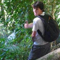 a young man with a backpack is standing on a log in the woods pointing at something