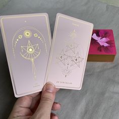 two pink cards with gold foil designs are being held by a person's hand