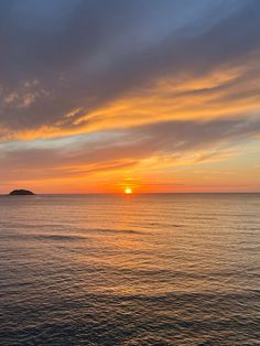 the sun is setting over an island in the middle of the ocean, with clouds