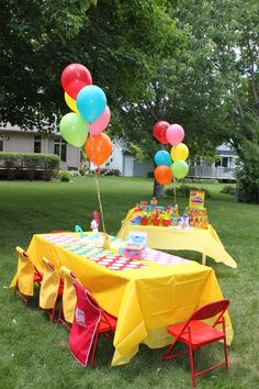 a table set up for a birthday party in the grass with balloons and candy on it