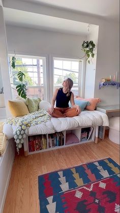 a woman sitting on top of a white couch in a living room next to a window