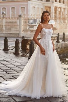 a woman in a white wedding dress standing on a brick walkway with her hand on her hip