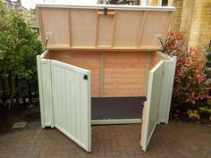 an outdoor wooden storage shed with its doors open on a brick patio next to shrubbery