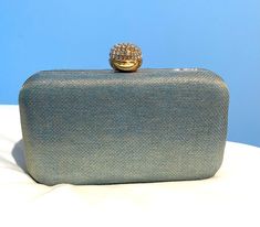 a blue purse with a gold ring on it sitting on a white cloth covered surface