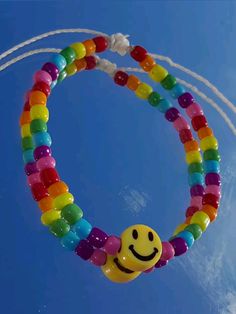 a smiley face beaded bracelet hanging from a string in the sky with white strings