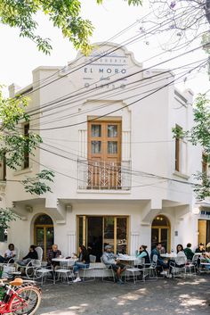 people sitting at tables in front of a white building with many windows and balconies