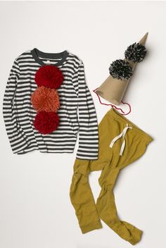 a child's outfit and hat are laid out on a white surface, including a striped sweater with red pom - poms