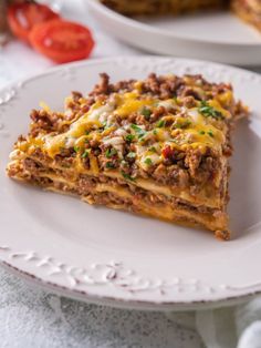 a slice of lasagna on a white plate with tomatoes in the back ground