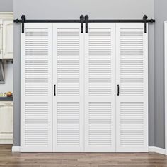 an open closet with white shutters and black hardware on the doors, against a gray wall