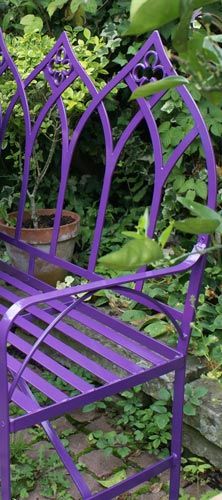 a purple metal chair sitting next to a bush