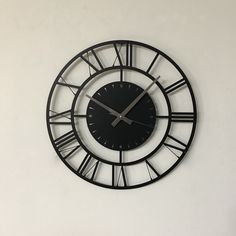 a black clock with roman numerals hanging on a white wall in a room