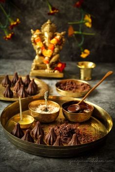 There is an idol of Ganesha in the backdrop. At the front is a brass plate with 7 chocolate modaks and a little bit of ghee in a bowl alongside grated coconut and melted dark chocolate. Chocolate Modak, Chocolate Money, Modak Recipe, Coconut Filling, Dry Coconut, Coconut Health Benefits, Dark Chocolate Bar, Indian Sweets, Milk Powder